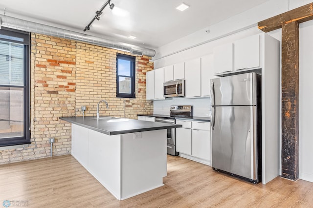 kitchen featuring sink, brick wall, kitchen peninsula, white cabinets, and appliances with stainless steel finishes