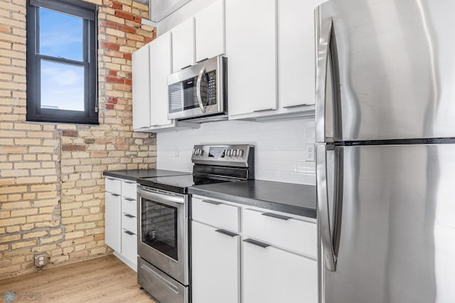 kitchen with light wood-type flooring, white cabinetry, stainless steel appliances, and brick wall