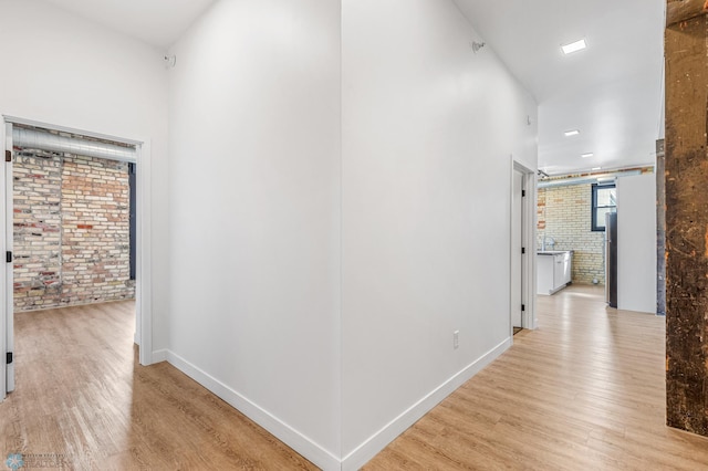 hall with light wood-type flooring and brick wall