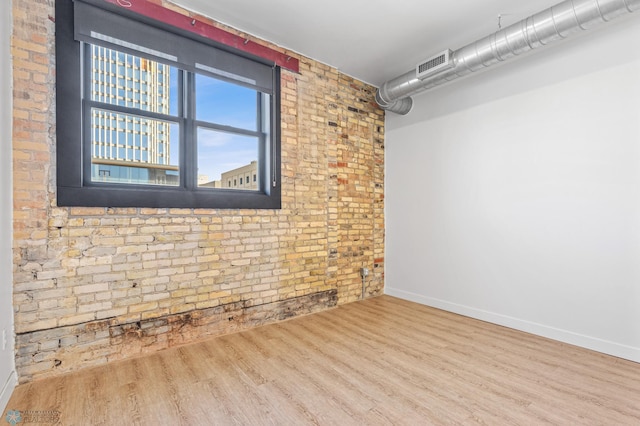 unfurnished room featuring wood-type flooring and brick wall