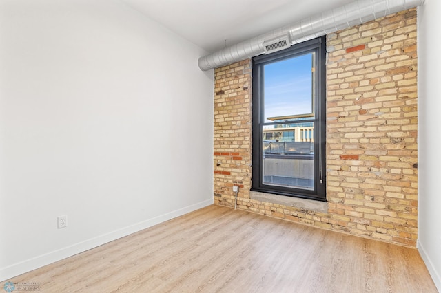 spare room with light hardwood / wood-style floors and brick wall