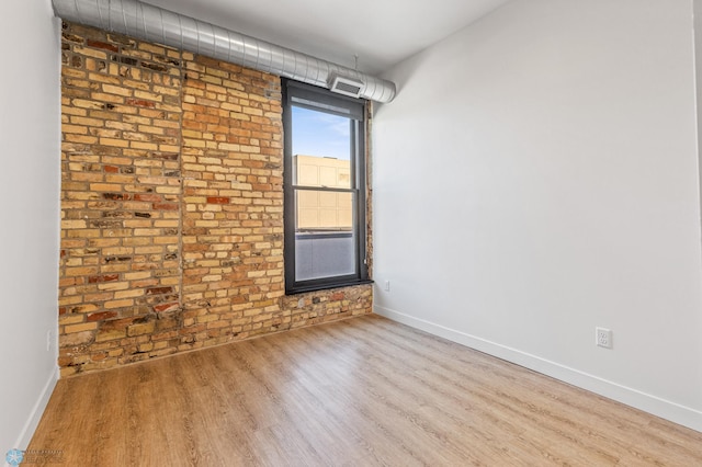 spare room with hardwood / wood-style flooring and brick wall