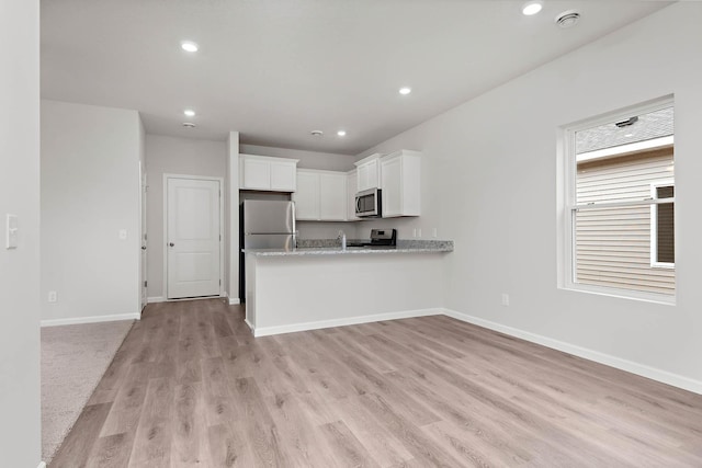 kitchen featuring light stone countertops, appliances with stainless steel finishes, kitchen peninsula, light hardwood / wood-style floors, and white cabinetry