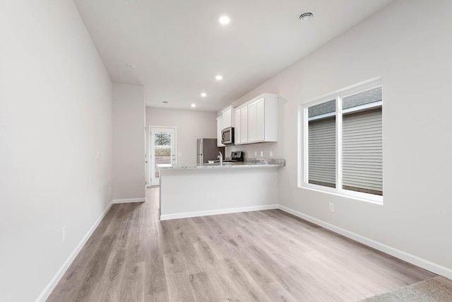 kitchen with kitchen peninsula, light stone countertops, light wood-type flooring, white cabinetry, and stainless steel appliances