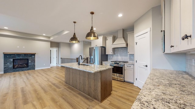 kitchen with light stone counters, white cabinetry, appliances with stainless steel finishes, custom range hood, and sink