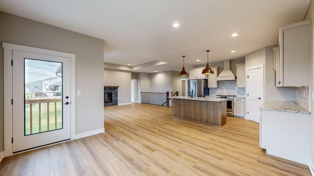 kitchen with stainless steel appliances, light hardwood / wood-style floors, custom range hood, a kitchen island, and pendant lighting