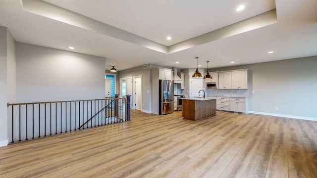 kitchen featuring a center island with sink, stainless steel appliances, decorative light fixtures, white cabinets, and light hardwood / wood-style flooring