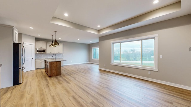 kitchen featuring light hardwood / wood-style floors, appliances with stainless steel finishes, light stone countertops, hanging light fixtures, and a kitchen island with sink