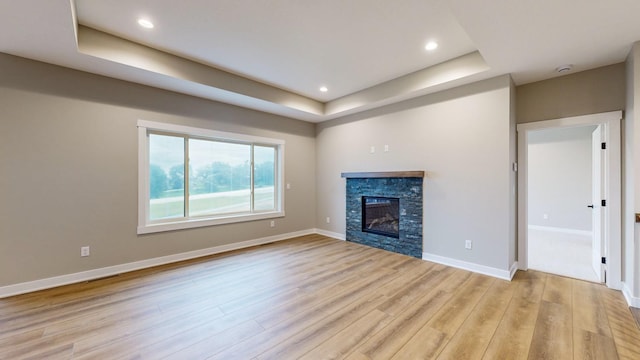 unfurnished living room with a stone fireplace, light hardwood / wood-style flooring, and a tray ceiling