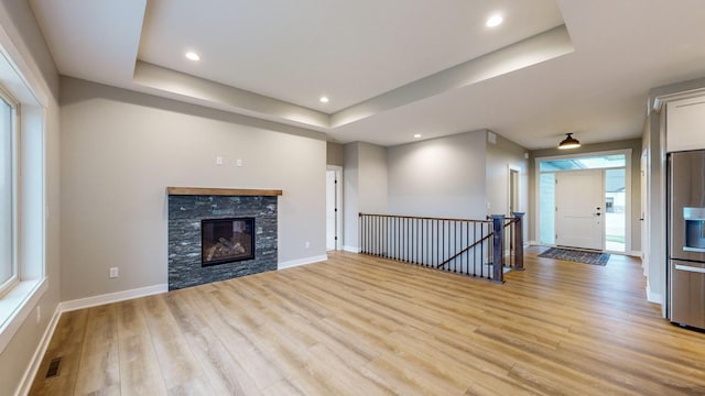 unfurnished living room with a stone fireplace, a raised ceiling, and light wood-type flooring