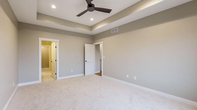 unfurnished bedroom with light carpet, ceiling fan, and a tray ceiling