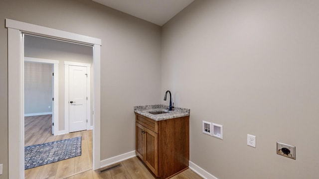 clothes washing area with light hardwood / wood-style flooring, washer hookup, sink, and hookup for an electric dryer