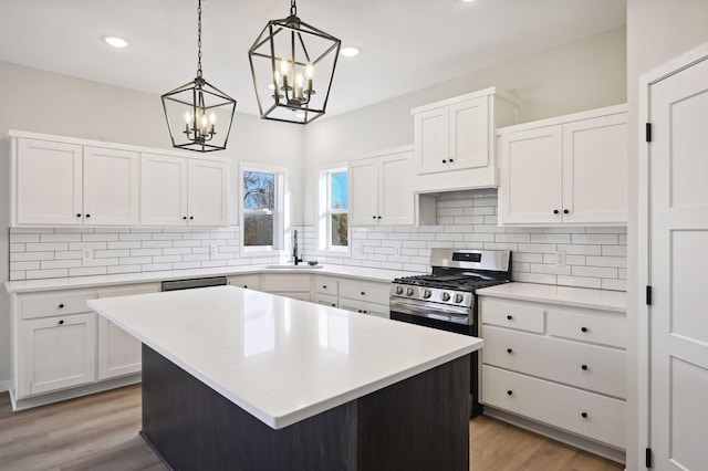 kitchen with gas stove, a kitchen island, white cabinetry, light wood-type flooring, and hanging light fixtures