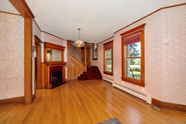 unfurnished living room with crown molding, light wood-type flooring, baseboard heating, a chandelier, and a textured ceiling