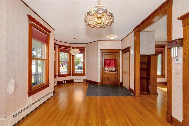 empty room with crown molding, baseboard heating, a notable chandelier, and light wood-type flooring