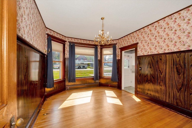 spare room featuring ornamental molding, wood walls, an inviting chandelier, a baseboard heating unit, and light hardwood / wood-style floors