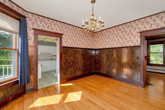 spare room with crown molding, plenty of natural light, wood-type flooring, and a chandelier