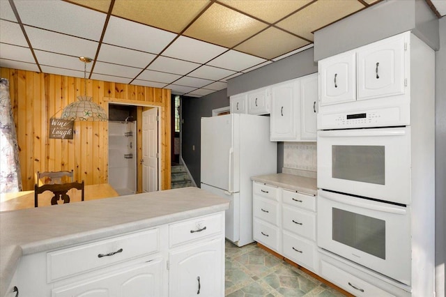 kitchen with white cabinets, white appliances, wooden walls, and a drop ceiling