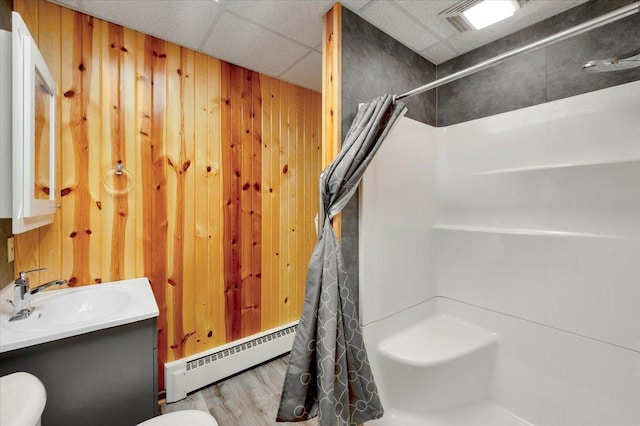 bathroom with toilet, a drop ceiling, vanity, a baseboard radiator, and hardwood / wood-style flooring