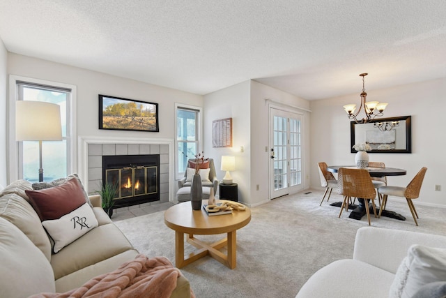 living room featuring light carpet, a healthy amount of sunlight, a tiled fireplace, a notable chandelier, and a textured ceiling