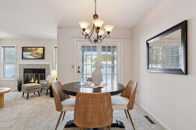 carpeted dining area featuring a tile fireplace and an inviting chandelier