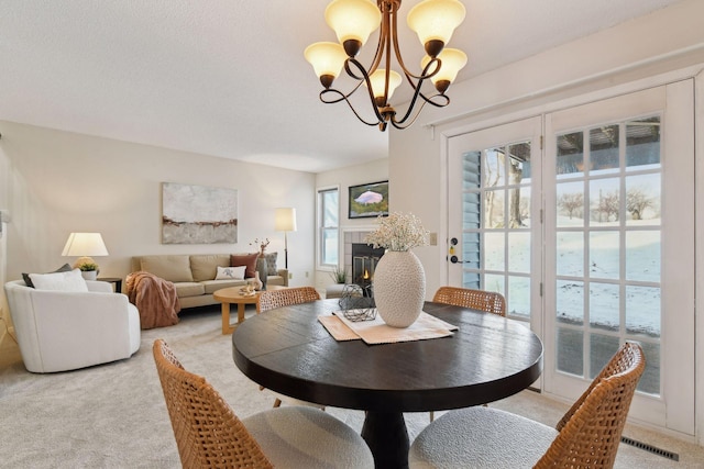 dining space with light carpet, a tile fireplace, and a notable chandelier