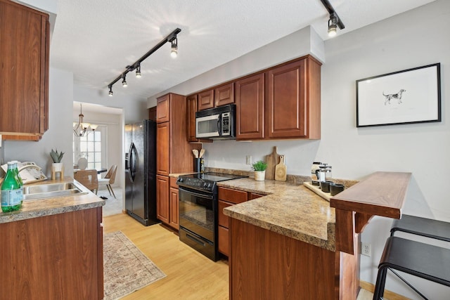 kitchen with black appliances, kitchen peninsula, sink, an inviting chandelier, and light hardwood / wood-style flooring