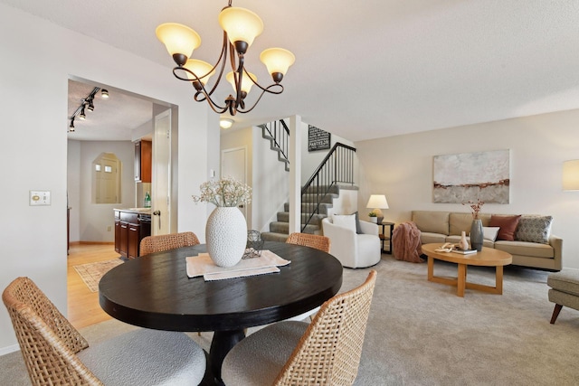 dining area with rail lighting, light colored carpet, and an inviting chandelier