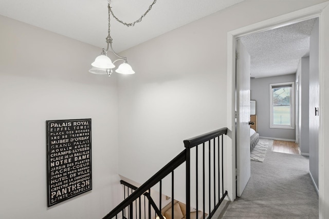 hall featuring a textured ceiling, light carpet, and a notable chandelier