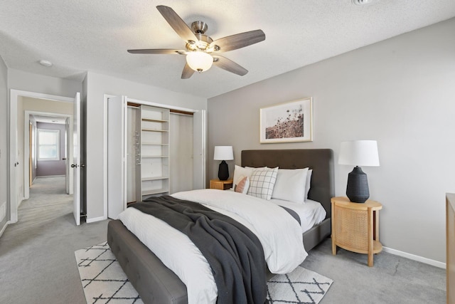 bedroom featuring a textured ceiling, ceiling fan, a closet, and light colored carpet