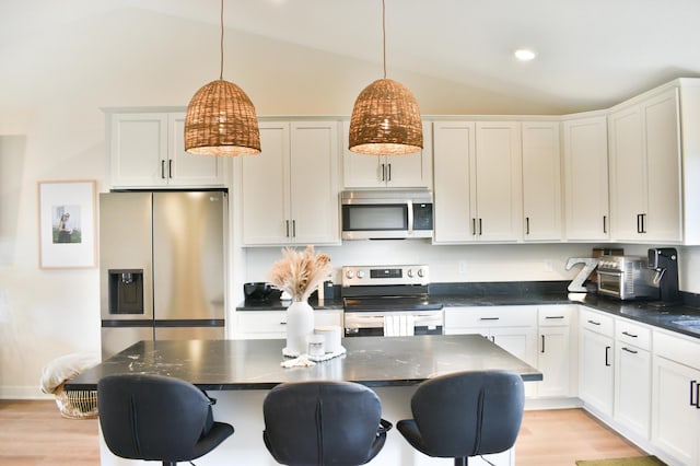 kitchen with lofted ceiling, decorative light fixtures, stainless steel appliances, and white cabinetry