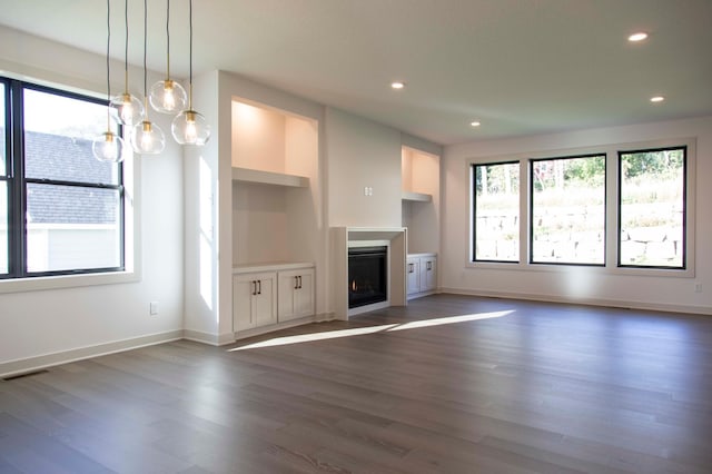 unfurnished living room featuring dark wood-type flooring, built in features, and a notable chandelier