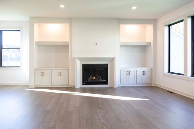 unfurnished living room featuring built in features and light hardwood / wood-style floors