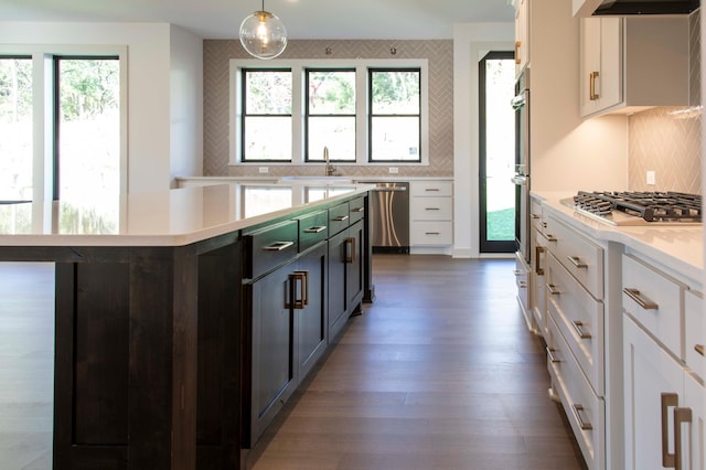 kitchen featuring white cabinets, decorative light fixtures, appliances with stainless steel finishes, dark hardwood / wood-style floors, and a center island