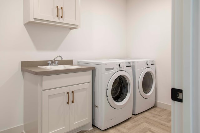 clothes washing area featuring cabinets, sink, washing machine and dryer, and light parquet floors