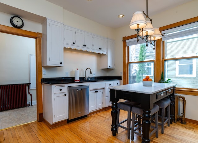 kitchen with stainless steel dishwasher, white cabinetry, light wood-type flooring, and hanging light fixtures