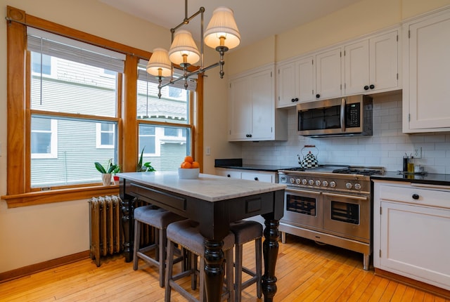 kitchen featuring white cabinets, appliances with stainless steel finishes, radiator heating unit, decorative light fixtures, and backsplash