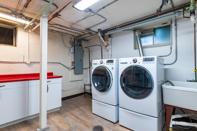 clothes washing area featuring sink, electric panel, washer and clothes dryer, and light hardwood / wood-style floors