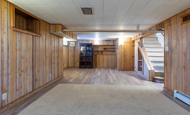 basement with wood walls, baseboard heating, and wood-type flooring