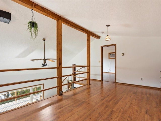 empty room featuring a wall unit AC, a textured ceiling, vaulted ceiling with beams, hardwood / wood-style floors, and ceiling fan