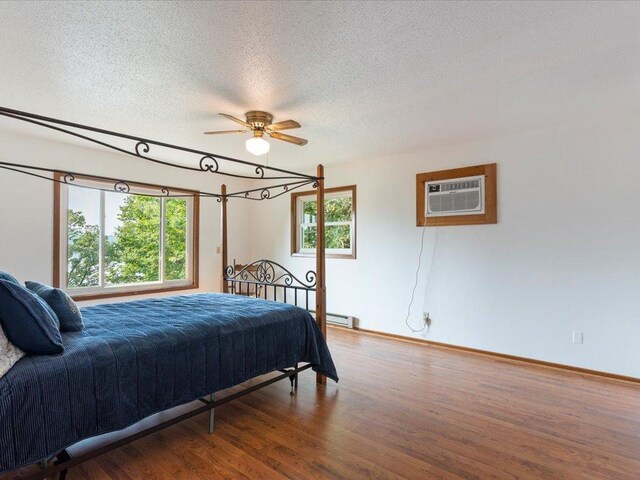 bedroom with multiple windows, a wall mounted AC, ceiling fan, and hardwood / wood-style flooring