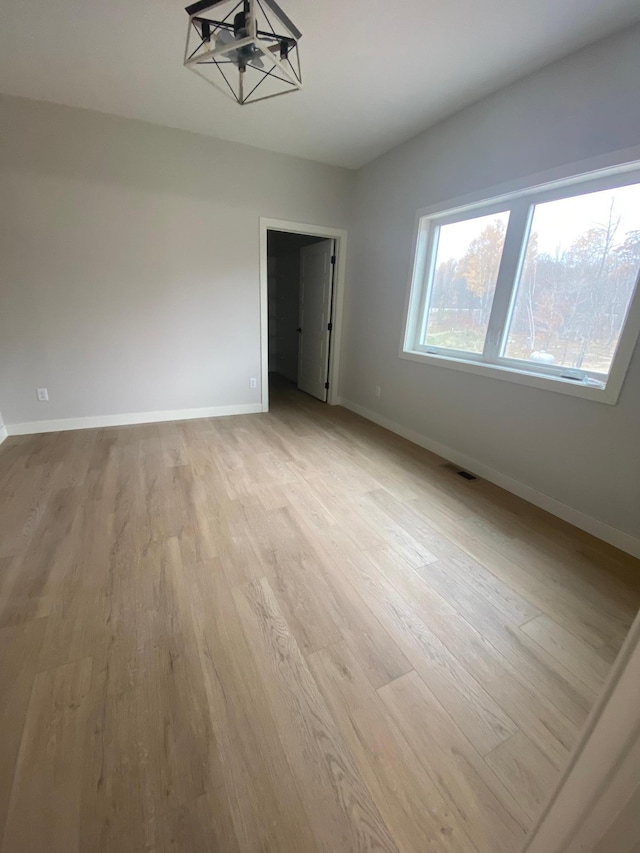 unfurnished room featuring a notable chandelier and light wood-type flooring