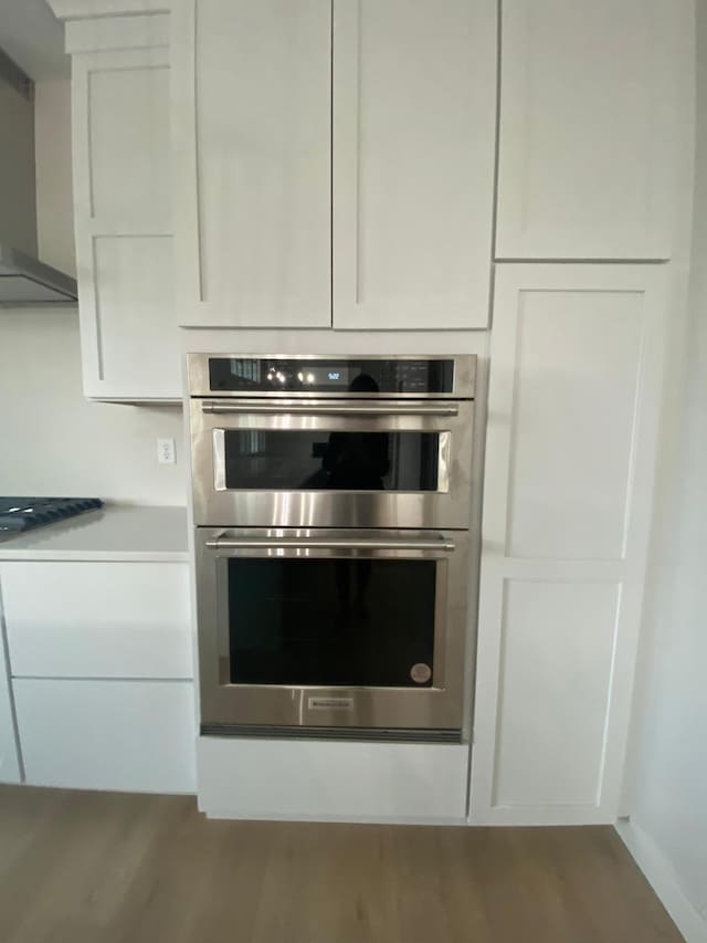 kitchen featuring white cabinetry, stainless steel double oven, hardwood / wood-style flooring, black gas cooktop, and wall chimney exhaust hood