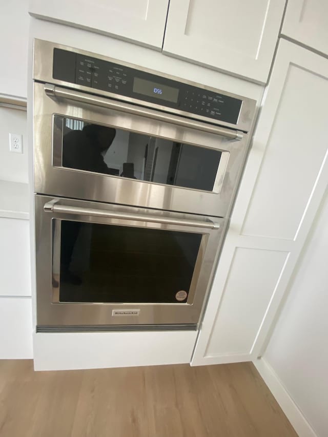 room details with double oven, white cabinets, and light hardwood / wood-style flooring