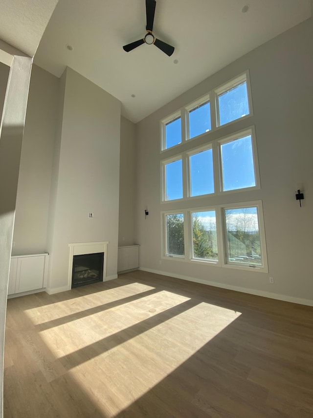 unfurnished living room featuring a wealth of natural light, a towering ceiling, and hardwood / wood-style flooring