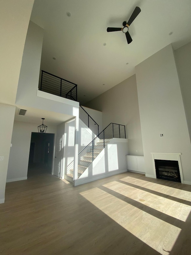 unfurnished living room featuring a towering ceiling, wood-type flooring, and ceiling fan