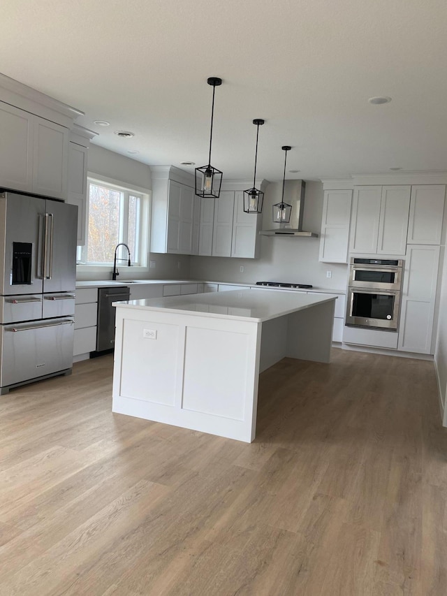 kitchen featuring light hardwood / wood-style floors, decorative light fixtures, a kitchen island, wall chimney range hood, and appliances with stainless steel finishes