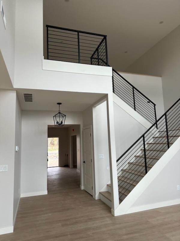 stairs featuring a towering ceiling, wood-type flooring, and a notable chandelier