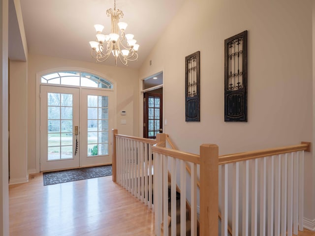 foyer featuring french doors, light hardwood / wood-style floors, lofted ceiling, and a notable chandelier