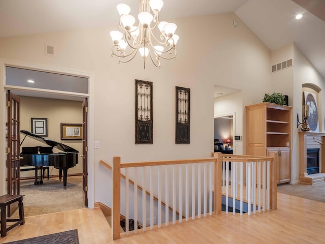 hallway with light hardwood / wood-style floors, high vaulted ceiling, and an inviting chandelier